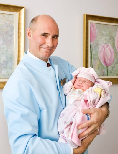 Gynecologist and IVF specialist Andrei Soritsa smiling, looking directly into the camera, holding a baby girl in his hands.