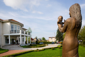 Elite clinic's garden in the summer. In the foreground there is a sculpture "Mother and child", in the background we can see the clinic."