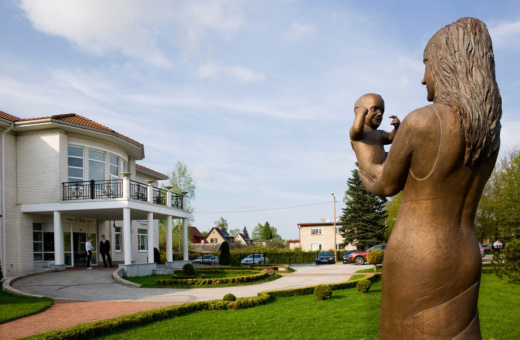 Elite clinic's garden in the summer. In the foreground there is a sculpture "Mother and child", in the background we can see the clinic."